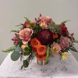 Mixed bouquet of pink, orange, and red flowers in a low metal vase