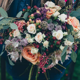 Bouquet of peach and white roses with purple accents and berries