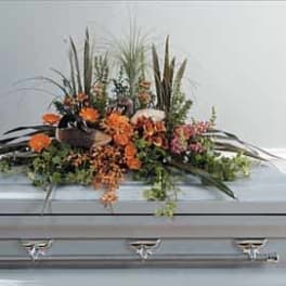 Orange floral casket spray with tall grasses and greenery