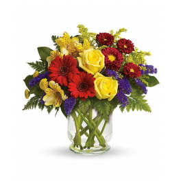 Mixed bouquet of yellow roses, red daisies, and purple filler in a clear glass vase