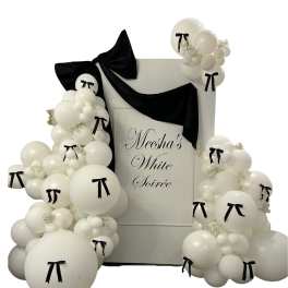 White balloon arch with black bows around a sign reading "Meesha's White Soirée"