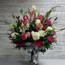 Pink and white floral arrangement in a glass vase with a checkered ribbon