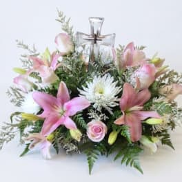 Pink lilies and white flowers arranged around a clear glass cross