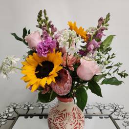 Mixed bouquet with sunflowers, pink roses, and purple blooms in a decorative vase