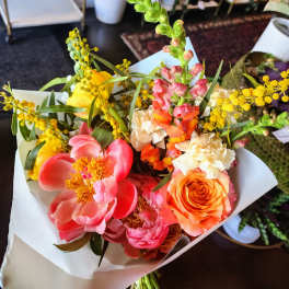 Bright mixed bouquet with pink, orange, yellow, and cream flowers wrapped in white paper