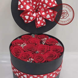 Red roses in a round black gift box with a heart-patterned ribbon bow