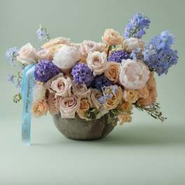 Pastel rose bouquet in a round vase with a blue ribbon