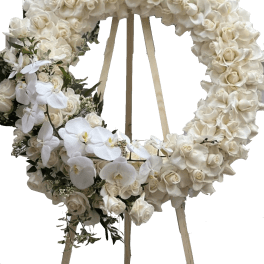 White floral wreath on a wooden easel with orchids and roses