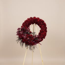 Red rose funeral wreath on a standing easel with dark purple accents