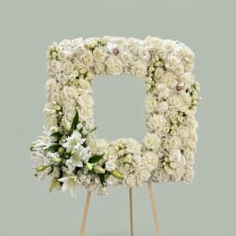 White floral wreath on a wooden easel with lilies and roses