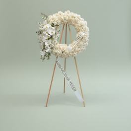 White floral wreath on a wooden easel with condolence ribbons