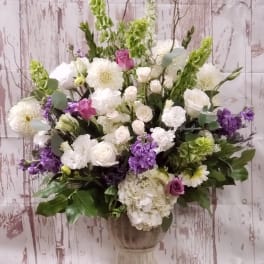 Large mixed floral arrangement in a pedestal vase with white, purple, and green blooms