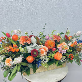 Low floral centerpiece with orange, pink, blue, and white blooms in a rectangular container