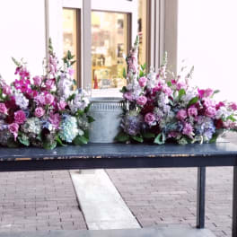 Two pink and lavender floral sprays flank a metal urn on a table