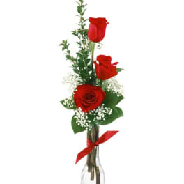 Three red roses in a clear glass vase with baby's breath and a red ribbon