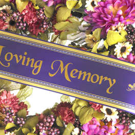 Purple memorial ribbon over a colorful floral wreath
