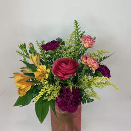 Mixed bouquet in a pink glass vase with bright pink, yellow, and purple flowers