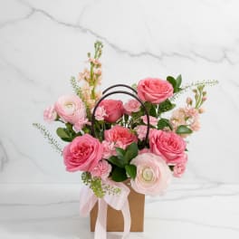 Pink roses and ranunculus arranged in a gift bag with a ribbon.