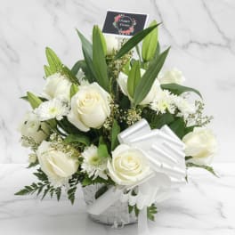 White roses and lilies arranged in a basket with a white ribbon