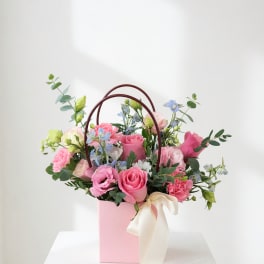 Pink and blue mixed flower arrangement in a pink gift box with ribbon handles