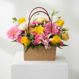 Mixed pink and yellow flowers arranged in a brown handled box