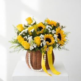 Yellow roses and sunflowers in a wicker basket with a yellow ribbon