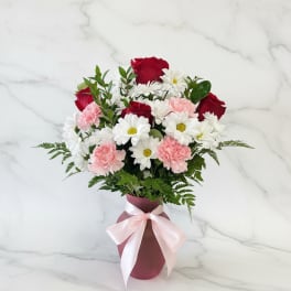 Bouquet of red roses, white daisies, and pink carnations in a pink vase