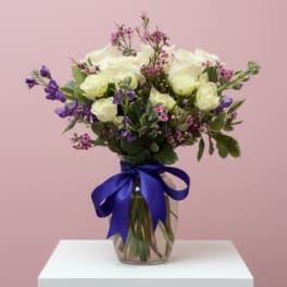 White and purple flower bouquet in a glass vase with a blue ribbon