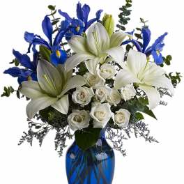 Arrangement of white lilies and roses with blue irises in a cobalt blue glass vase
