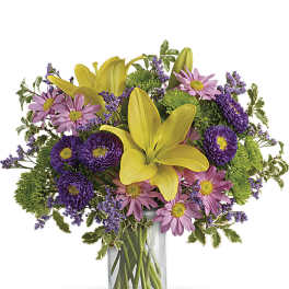 Yellow lilies with pink and purple daisies in a clear glass vase