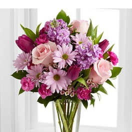 Mixed bouquet of pink roses, tulips, daisies, and stock in a tall clear glass vase