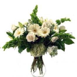 White gerbera daisies, roses, and hydrangea arranged in a clear glass vase