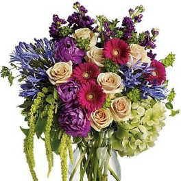 Tall mixed bouquet of purple, pink, cream, and green flowers in a clear glass vase
