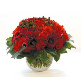 Low round arrangement of red roses in a clear glass bowl vase with a collar of glossy leaves.