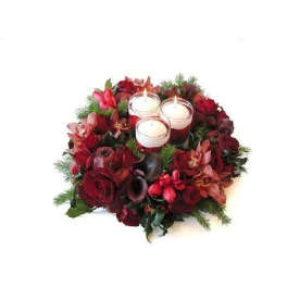 Round arrangement of dark red flowers with three white votive candles in glass at the center
