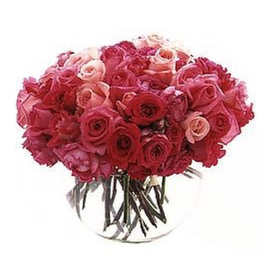Low arrangement of pink and red roses clustered tightly in a clear round glass vase