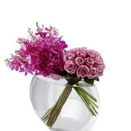 Modern arrangement of pink orchids and lavender roses in a clear round glass vase