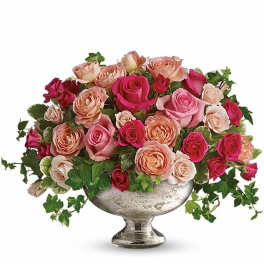 Low centerpiece of pink and peach roses in a silver pedestal bowl with trailing ivy