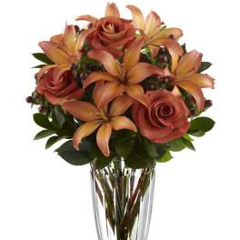 Clear vase with orange roses and lilies arranged in a compact bouquet