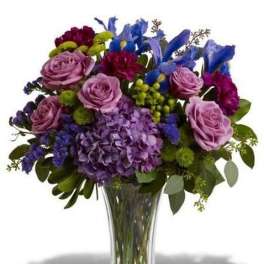 Purple and blue mixed flower arrangement with roses, hydrangea, and irises in a clear glass vase