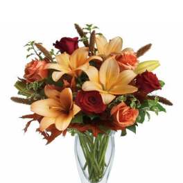 Glass vase of orange lilies with red and orange roses in a mixed fall-toned arrangement
