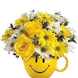 Yellow roses and white and yellow daisies arranged in a yellow smiley-face mug
