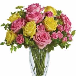 Tall clear vase of pink and yellow roses arranged in a mixed bouquet