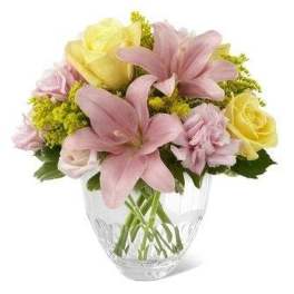 Pastel arrangement of pink lilies, yellow roses, and pink carnations in a clear glass vase