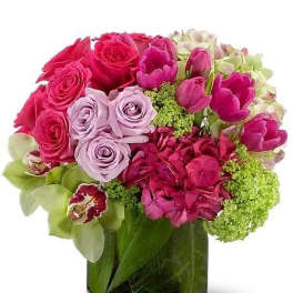 Compact arrangement of pink and lavender roses, tulips, hydrangeas and green orchids in a clear glass vase