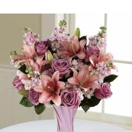 Pink lilies and purple roses arranged in a lavender glass vase
