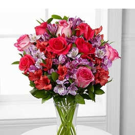 Tall glass vase of pink and red roses mixed with purple and white blooms