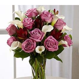 Tall glass vase of lavender roses, white calla lilies, and red accent blooms