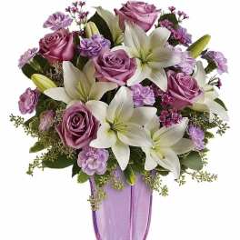 Tall arrangement of white lilies and lavender roses in a lavender glass vase