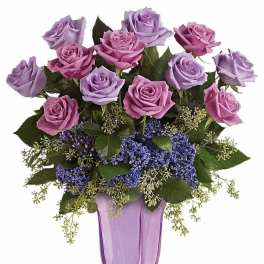 Tall arrangement of lavender and pink roses with purple filler flowers in a lavender glass vase